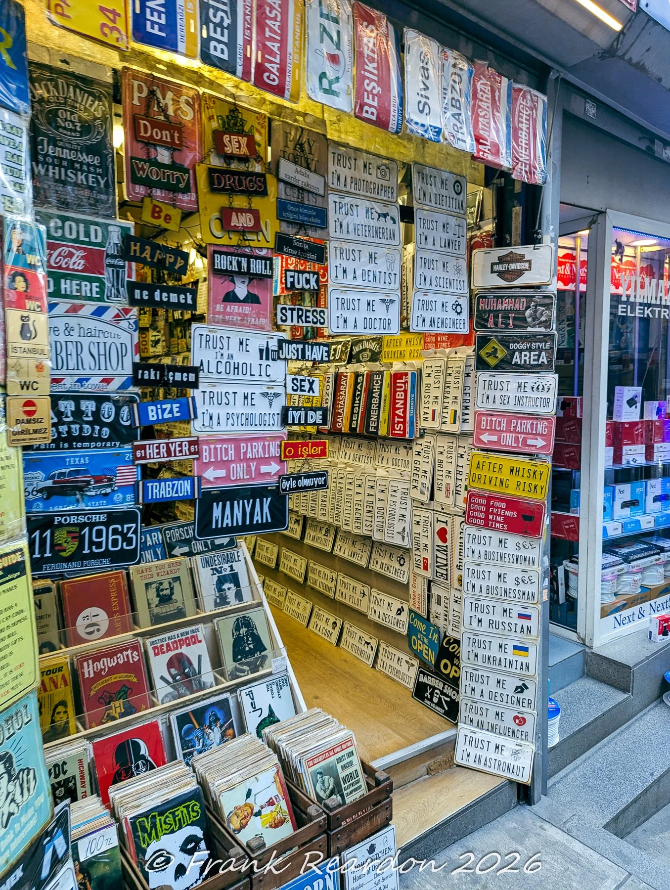 A close-up view of an array of witty quote signs, movie posters, and football club memorabilia hanging outside a shop.