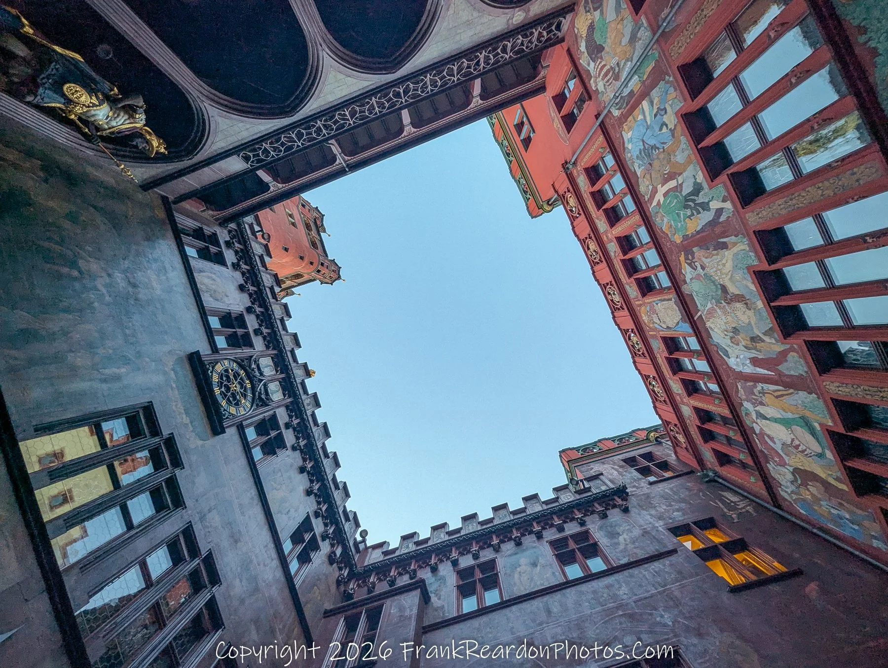 "Looking Up from the Courtyard" A low-angle, symmetrical perspective from within the inner courtyard of the Rathaus, capturing the ornate painted facades and the surrounding architecture against the clear sky.