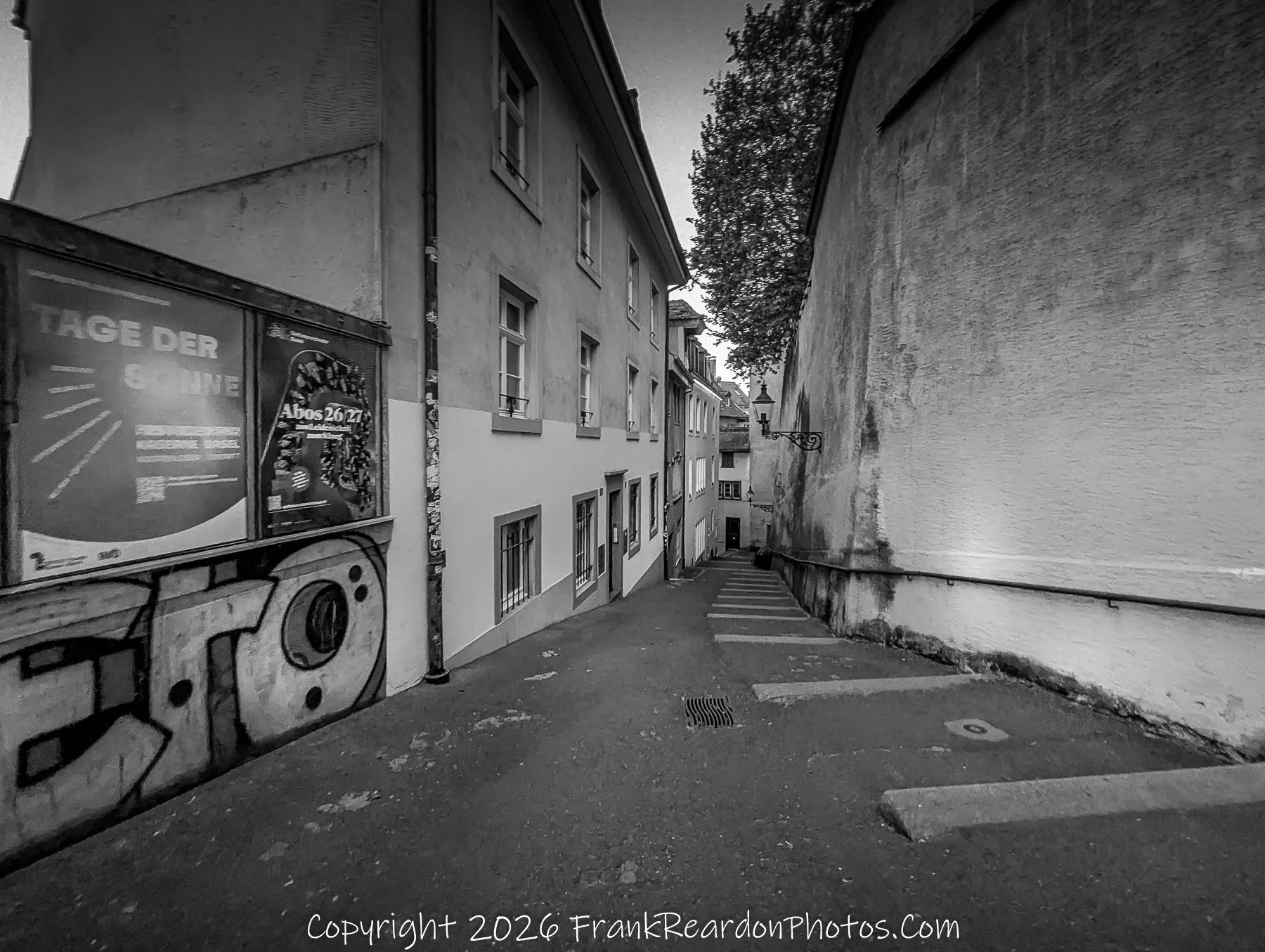 "The Quiet Passage" A narrow, black-and-white view of a steep, stepped alleyway bordered by historic buildings and a graffiti-covered wall.
