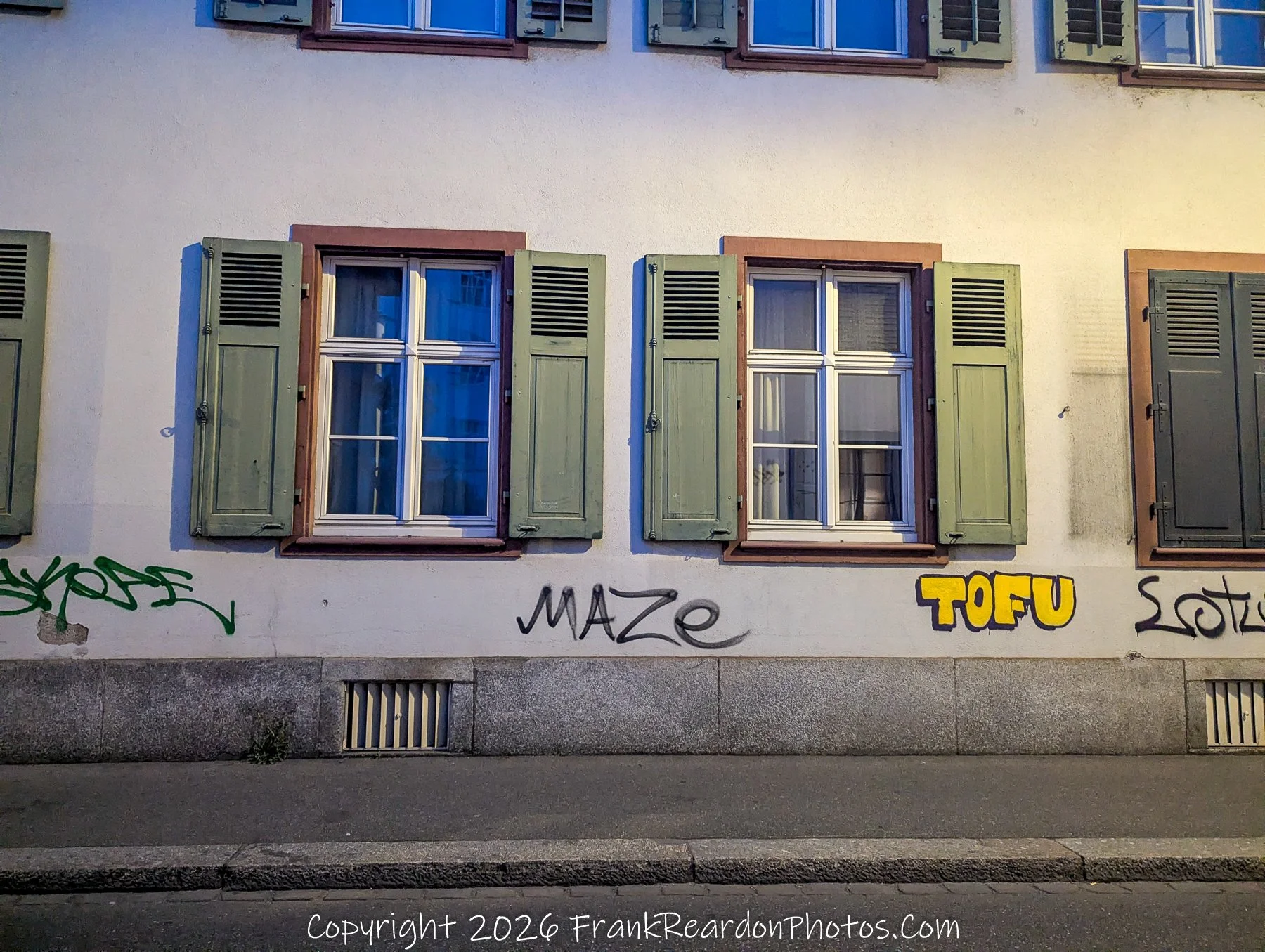 "Urban Texture" A wall featuring historic windows with green shutters, contrasted by modern street art and graffiti tags at street level.