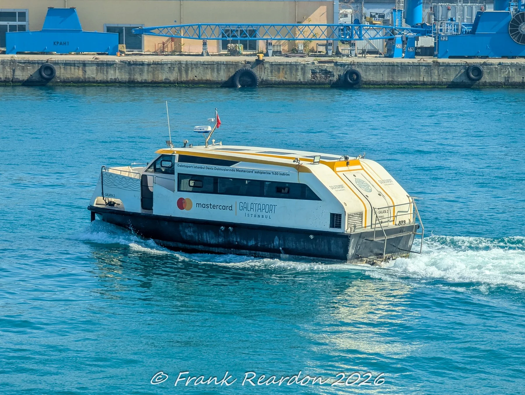 A sleek, modern passenger water taxi branded with Galataport Istanbul and Mastercard speeding across the blue waters of the strait.