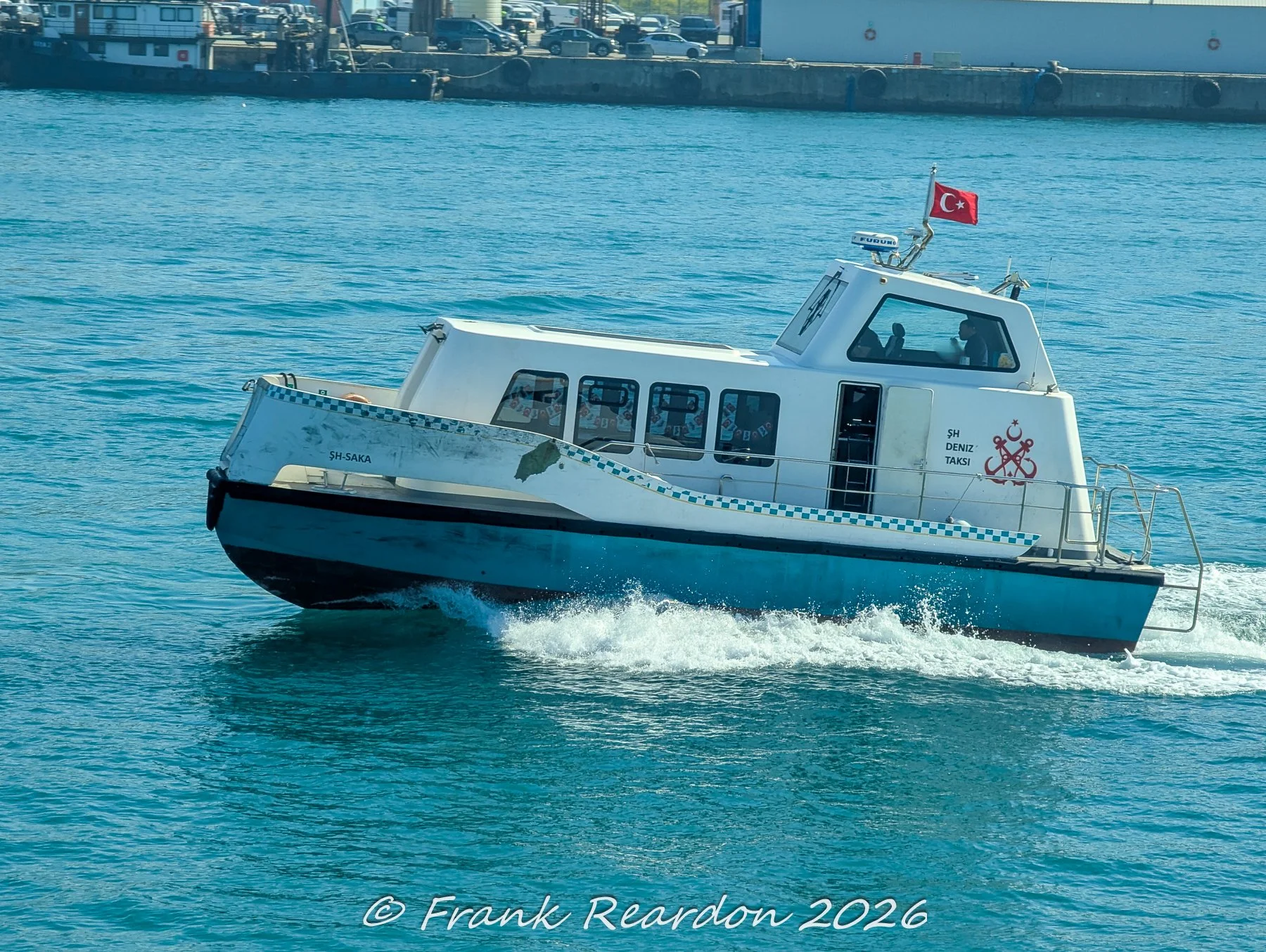 A white and blue municipal water taxi, ŞH-Saka, carving through the choppy Bosphorus waves near the Istanbul shoreline.