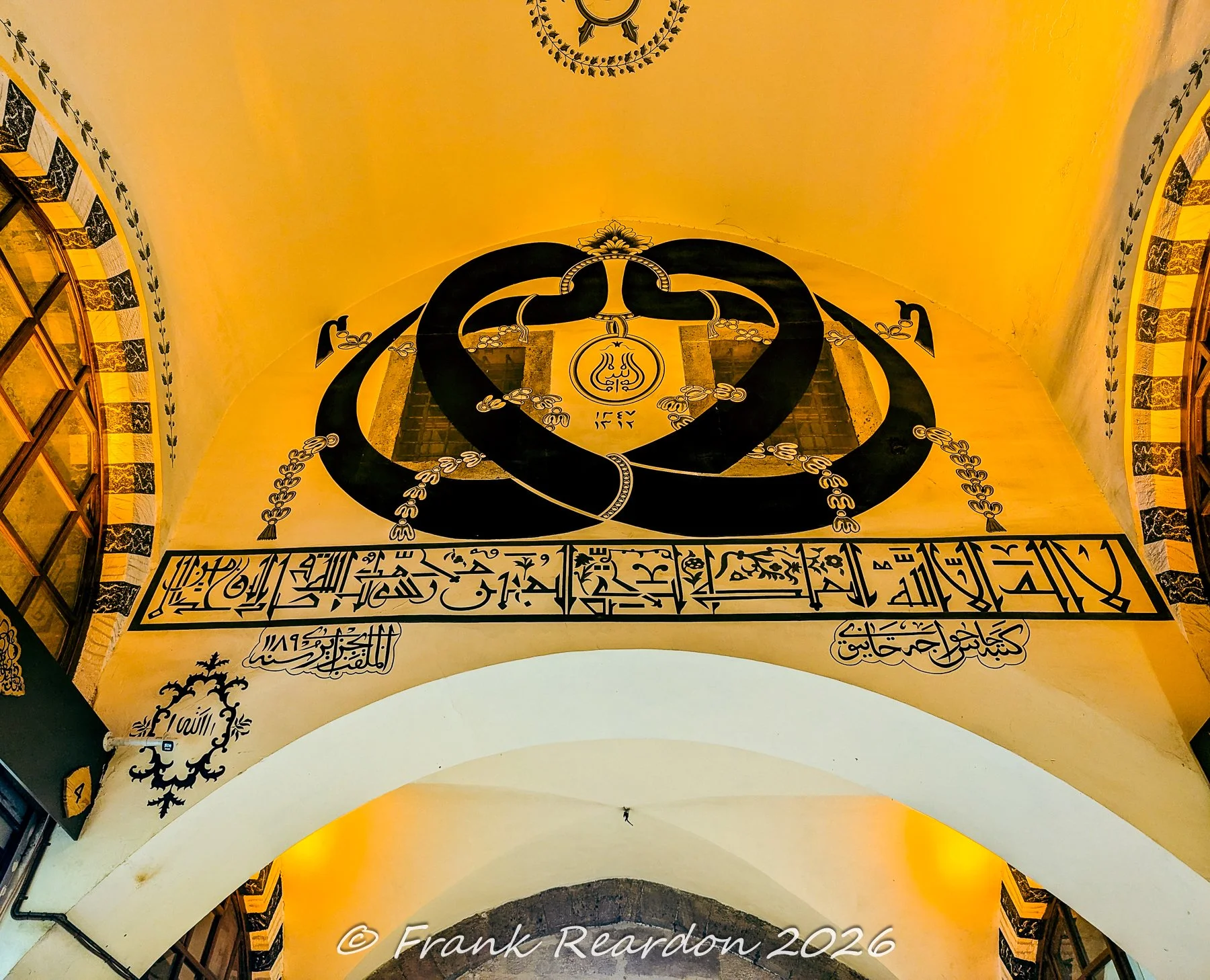 Ornate black Islamic calligraphy inscriptions and traditional decorative patterns painted on the yellow-toned walls of the Grand Bazaar.
