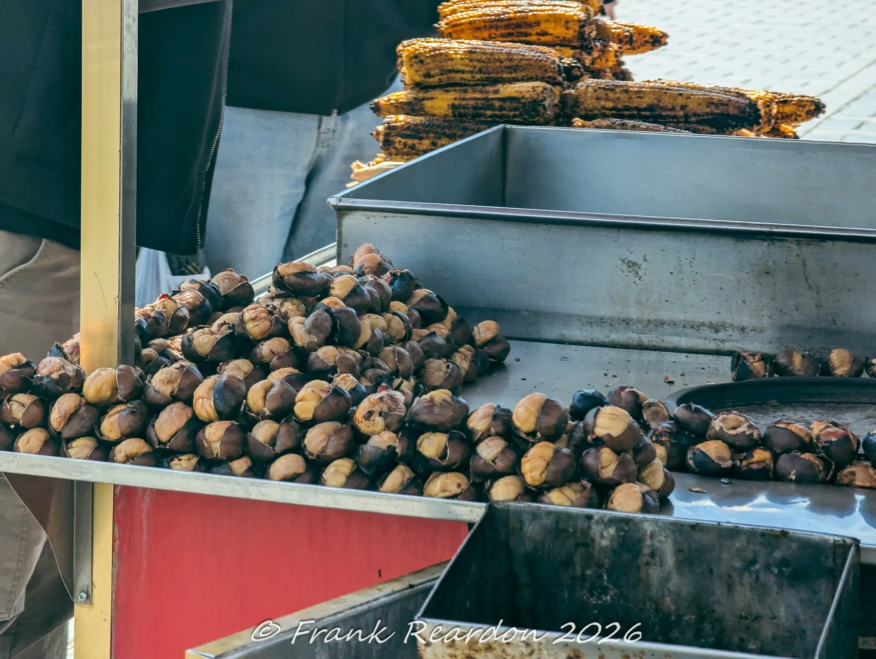 A close-up of a street food cart piled high with freshly roasted chestnuts and charred corn on the cob on an Istanbul street.