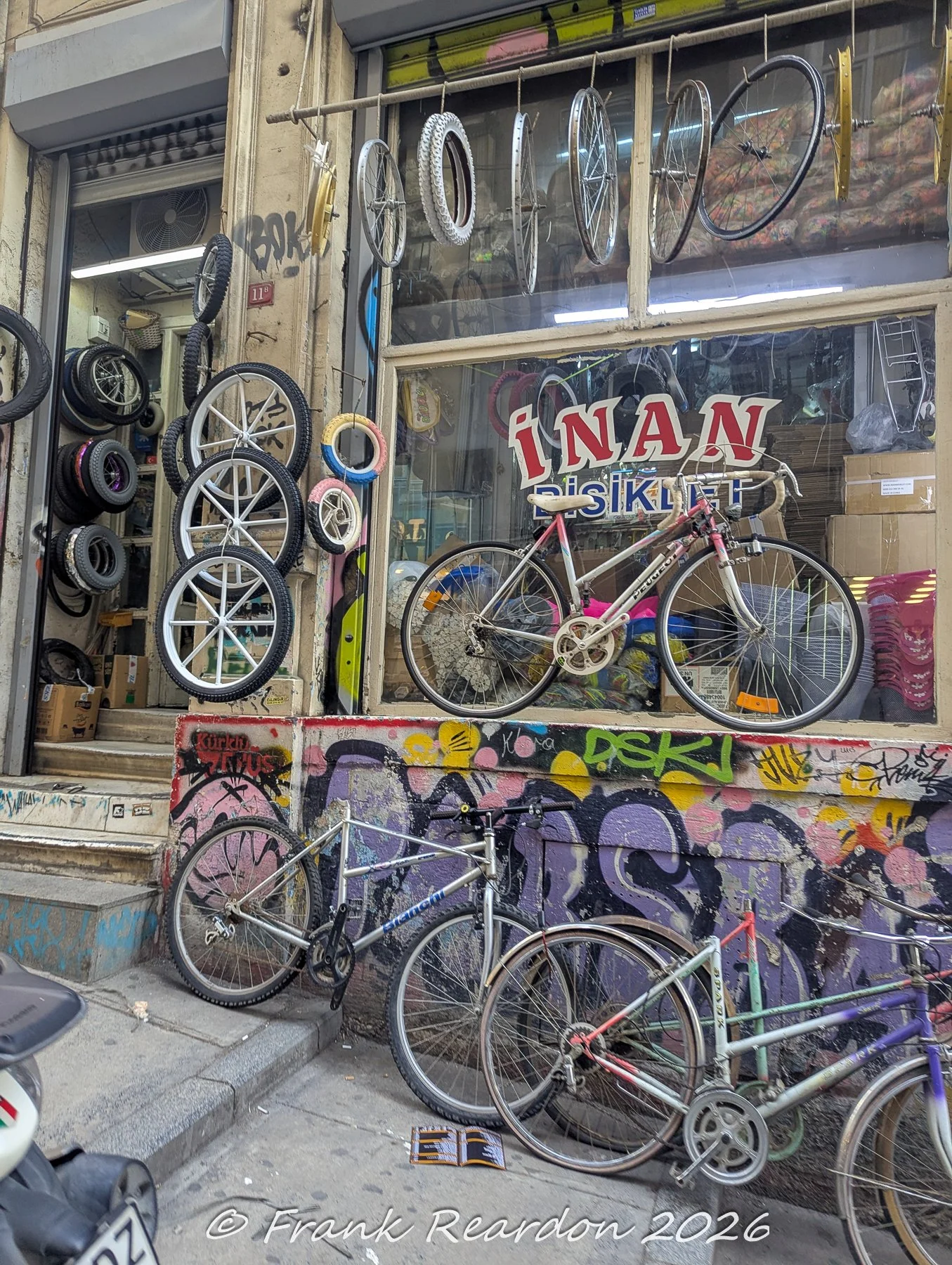 The storefront of İnan Bisiklet featuring bicycle wheels and parts mounted on the exterior walls, with various bikes parked along the colorful graffiti-covered base.