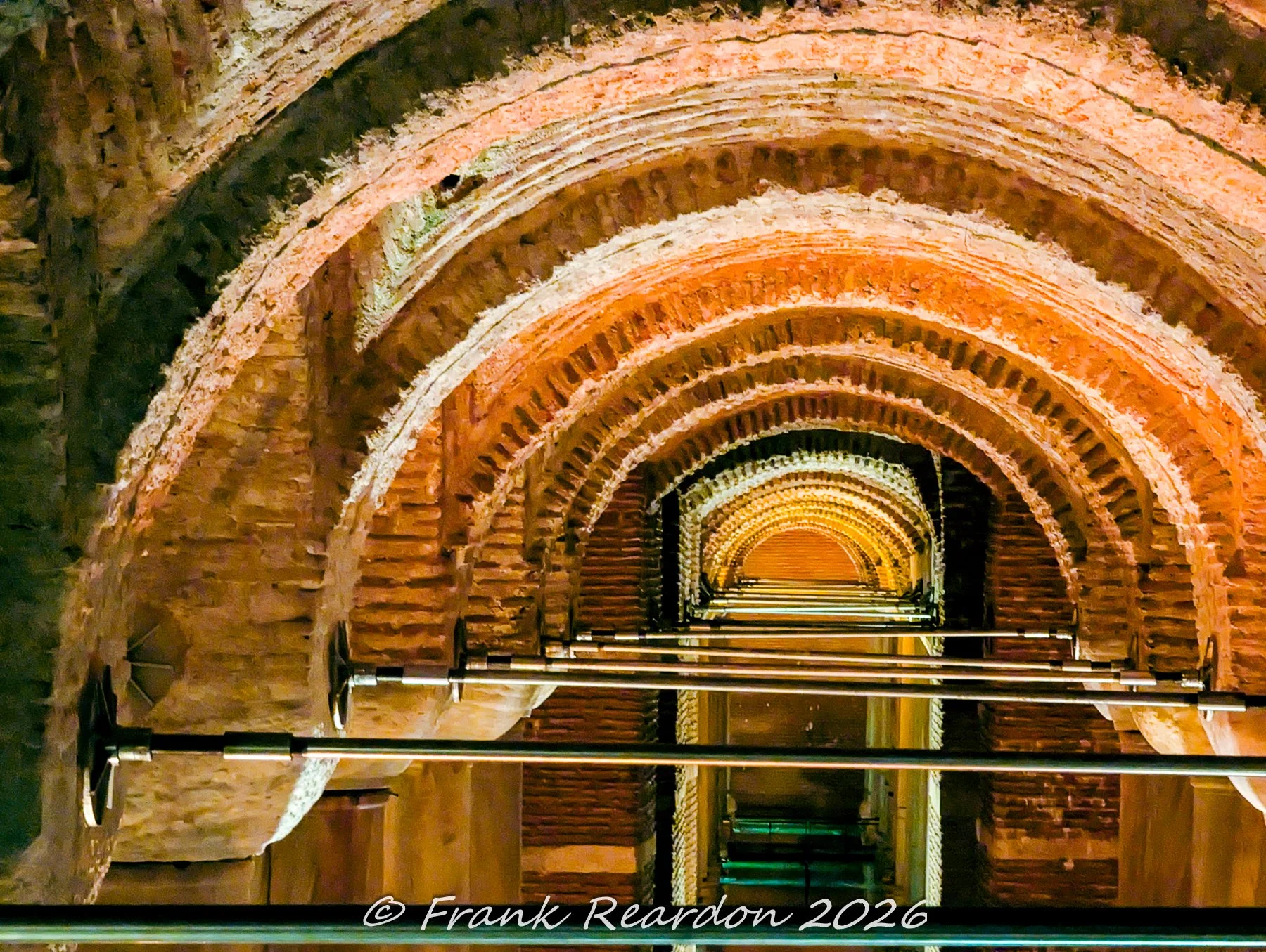 A close-up perspective looking up at the curved, amber-lit brick vaults and structural support rods inside the Basilica Cistern.