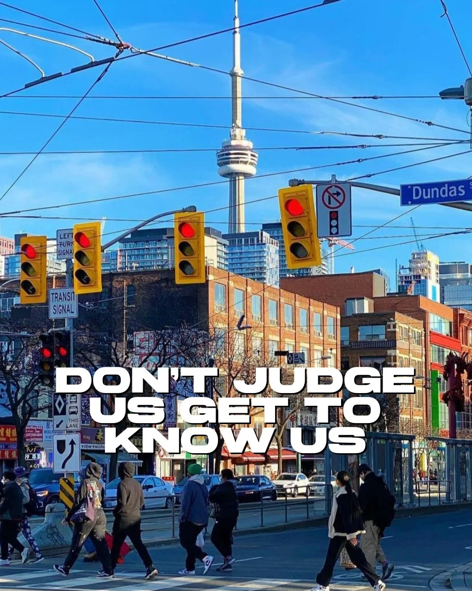 City street scene with pedestrians crossing and multiple traffic lights, Toronto CN Tower visible in the background, street sign indicating Dundas Street.
