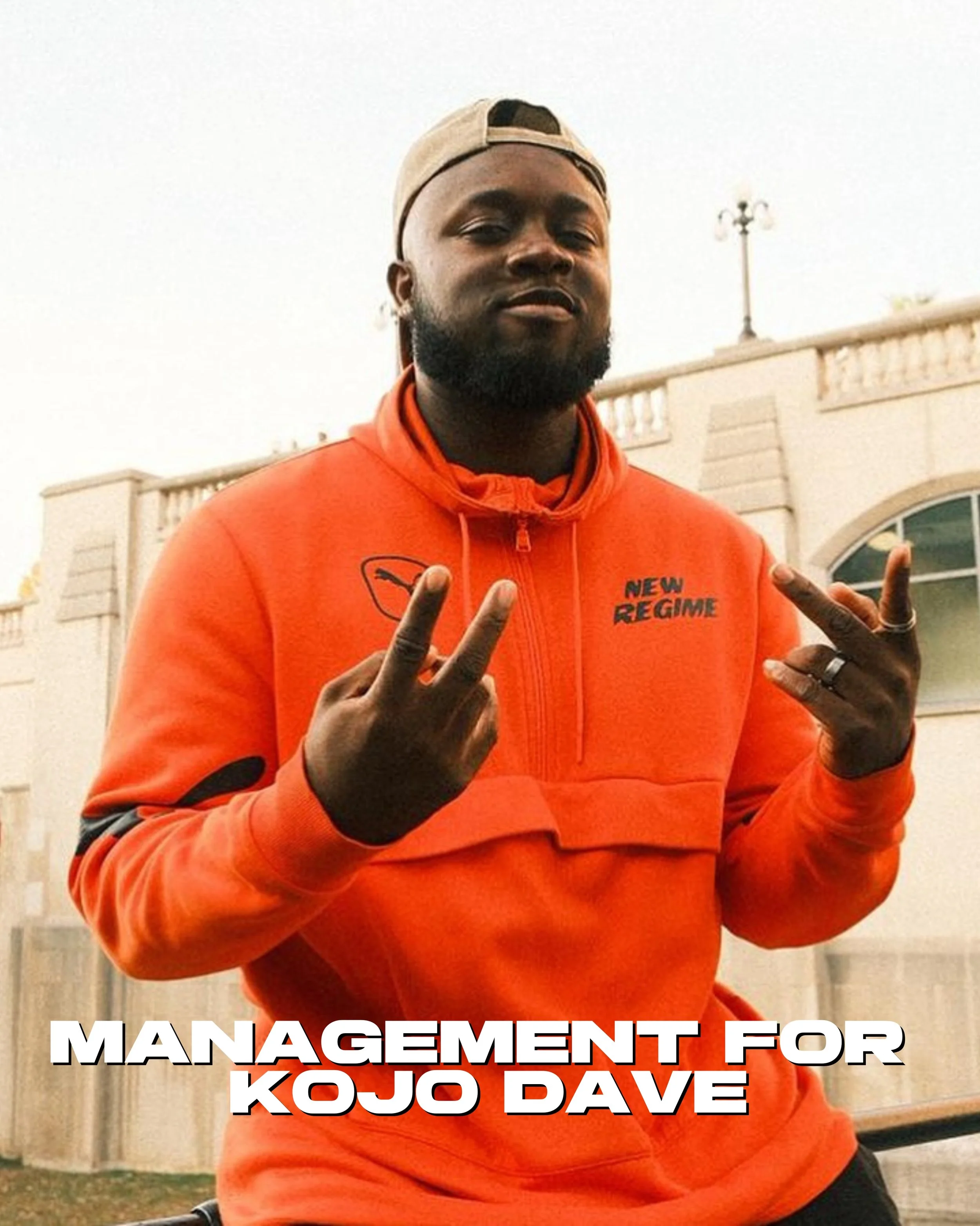 Kojo Dave in a red hoodie with the words 'NEW REGIME' on it making a peace sign with both hands.