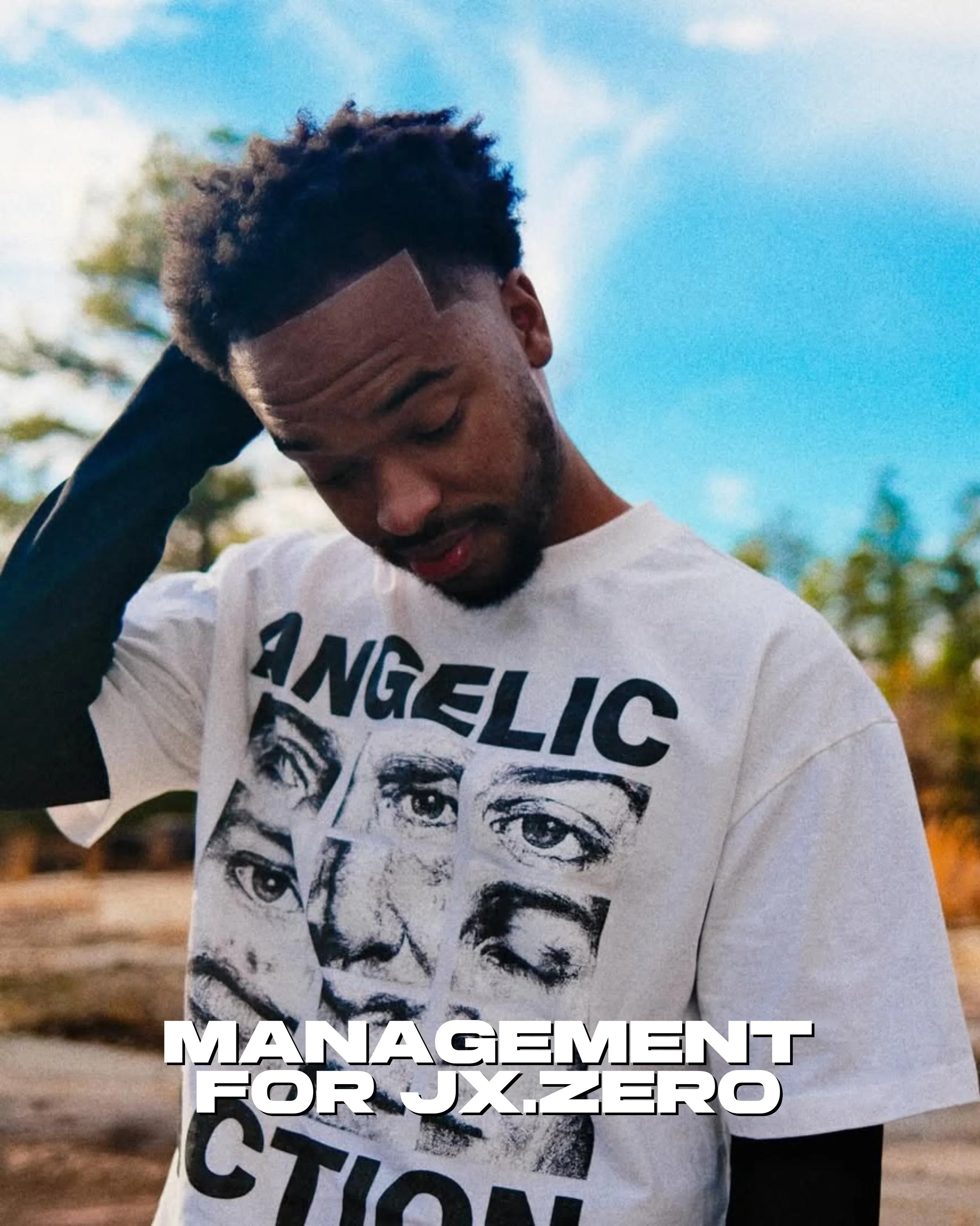 Jx.Zero wearing a graphic t-shirt with various face images and the words 'Angelic' and 'Action.' He is outdoors in a natural setting with trees and rocks, and is touching his hair with his right hand.