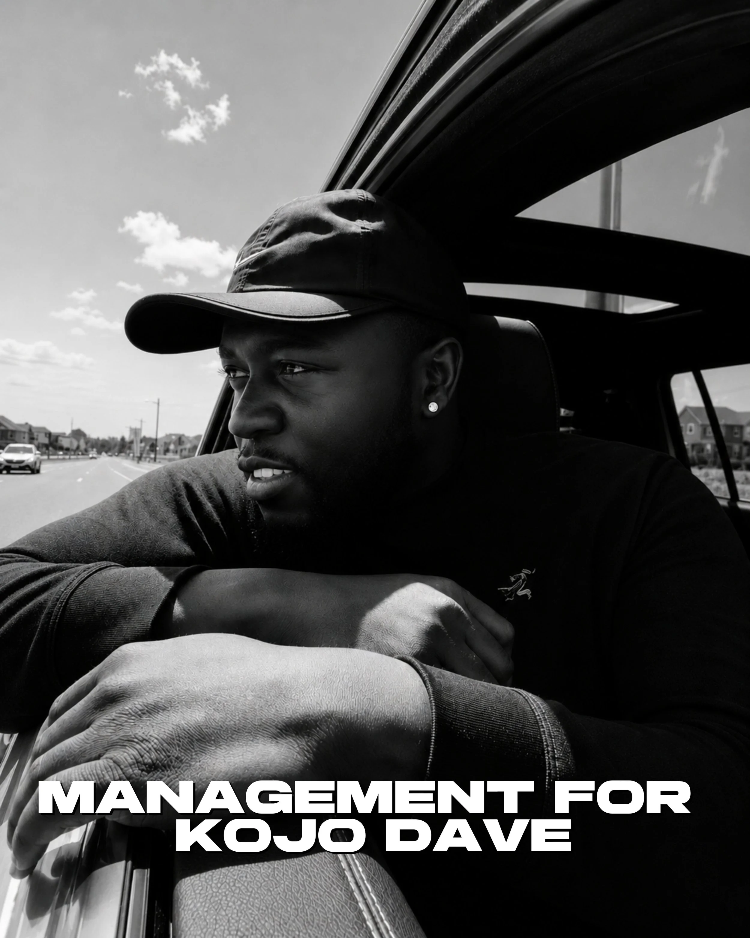 Black and white photo of a Kojo Dave wearing a cap and a jacket, sitting in a vehicle, with a background of a few buildings and a road, and a partial view of some text about management for Kojo Dave.