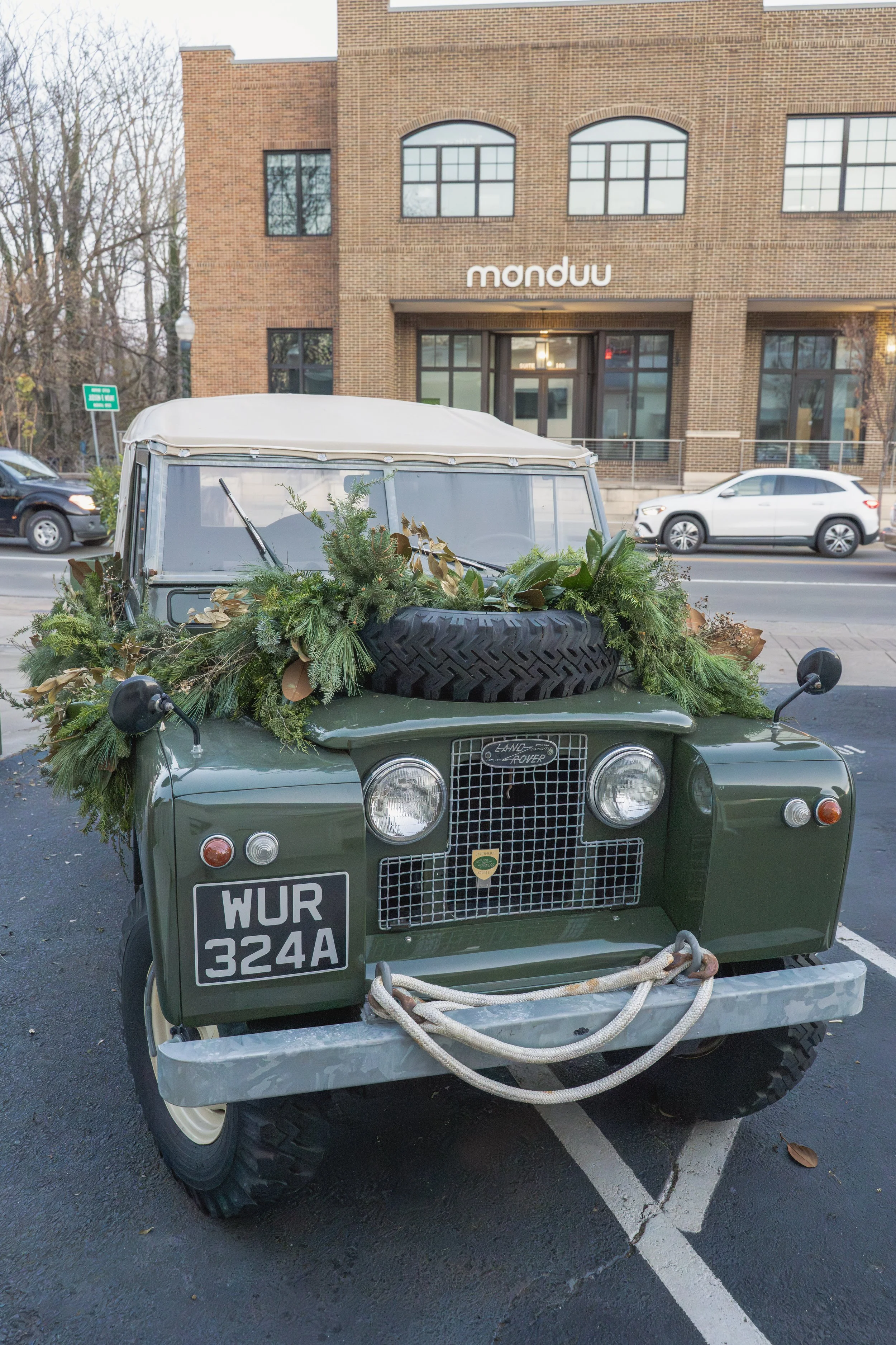 Front view of a vintage green Land Rover dressed with Christmas greenery across its hood and windshield.