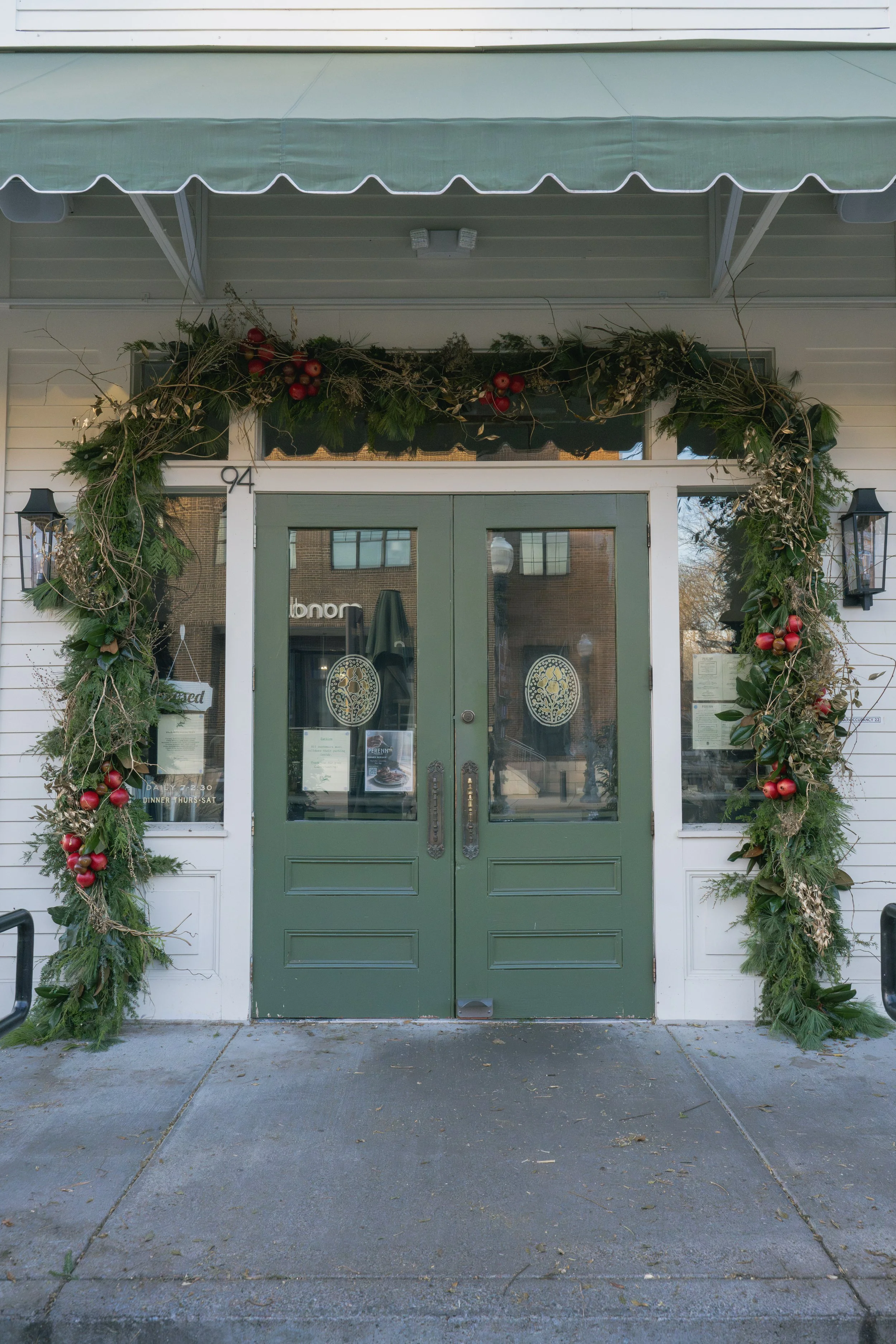 Evergreen Christmas garlands surrounding Perenn’s double green doors beneath a scalloped green awning.