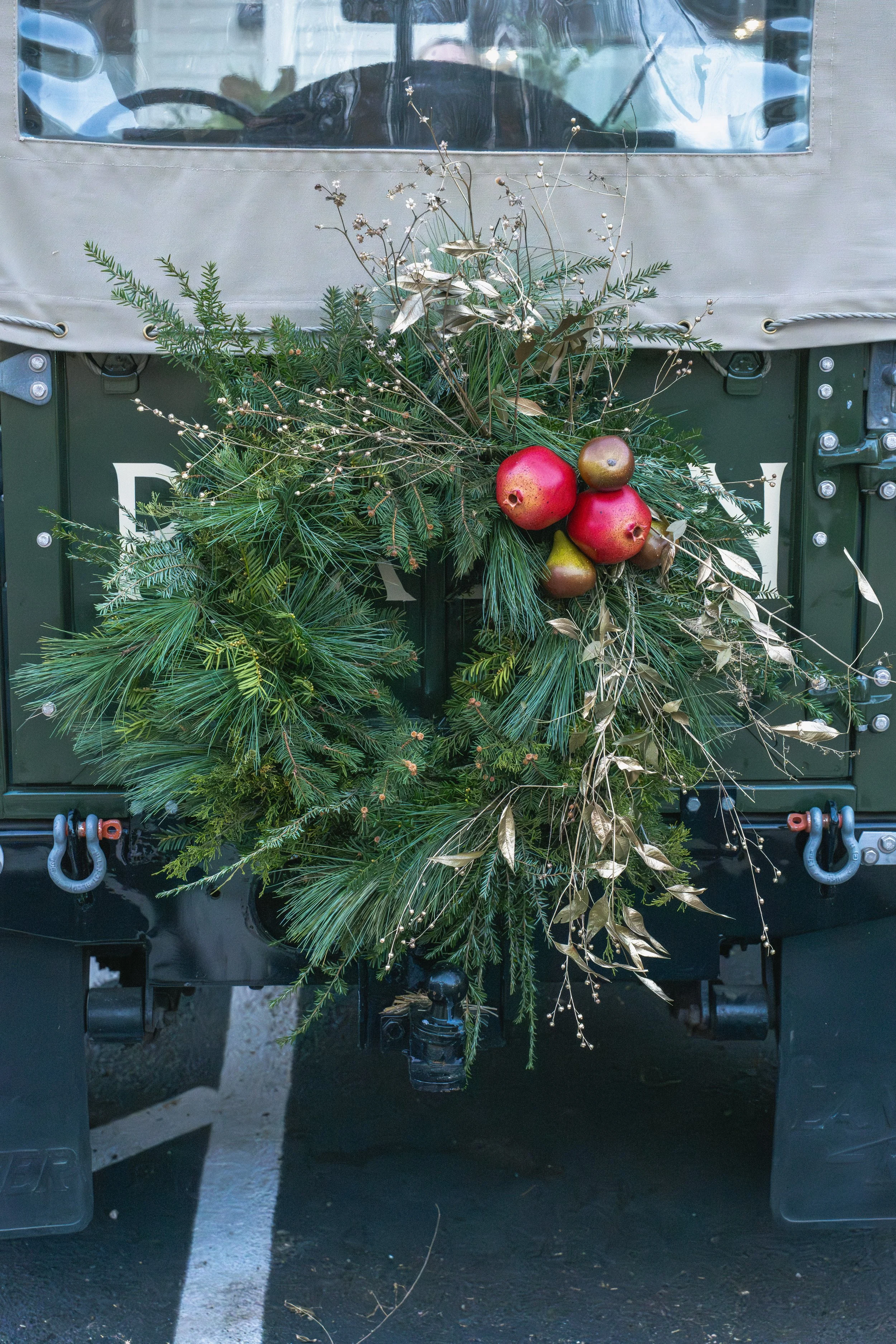 Asymmetrical evergreen wreath with pomegranates, pears, and fine branching stems on the rear of a vintage Land Rover.