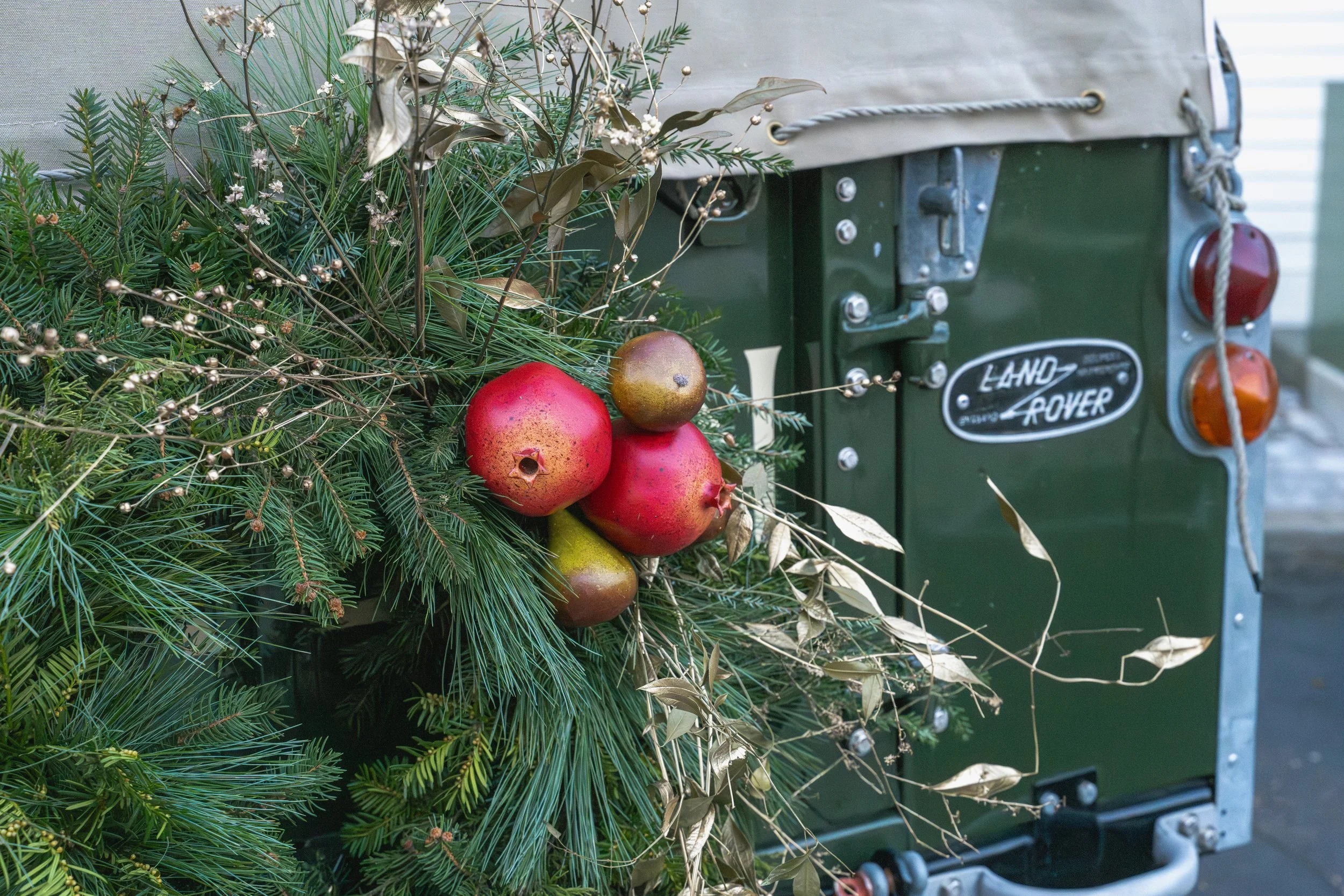 Close view of red pomegranates and pears among layered evergreen foliage on the Land Rover’s Christmas wreath.