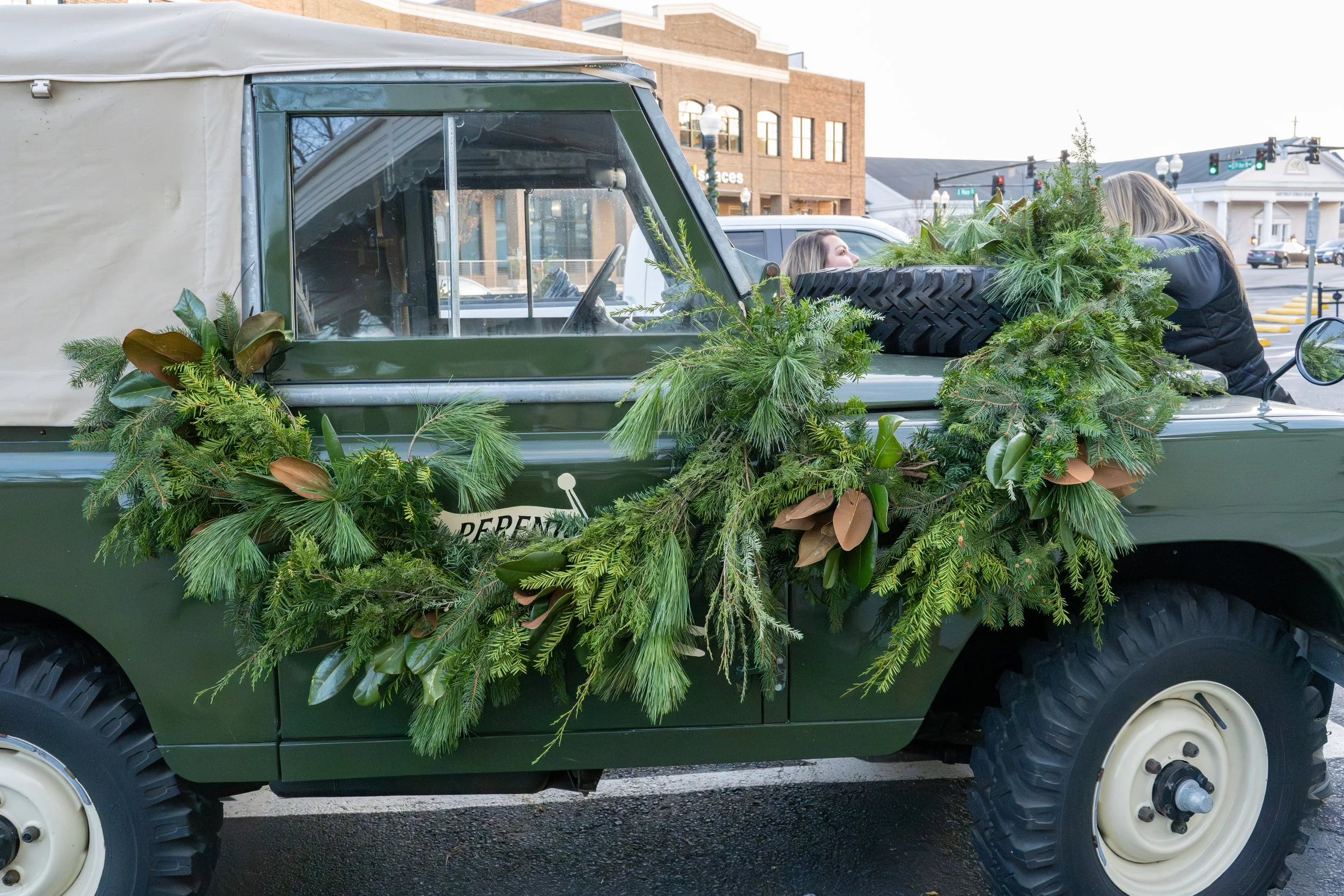 Vintage green Land Rover decorated with generous evergreen garlands, magnolia foliage, and fruit outside Perenn.
