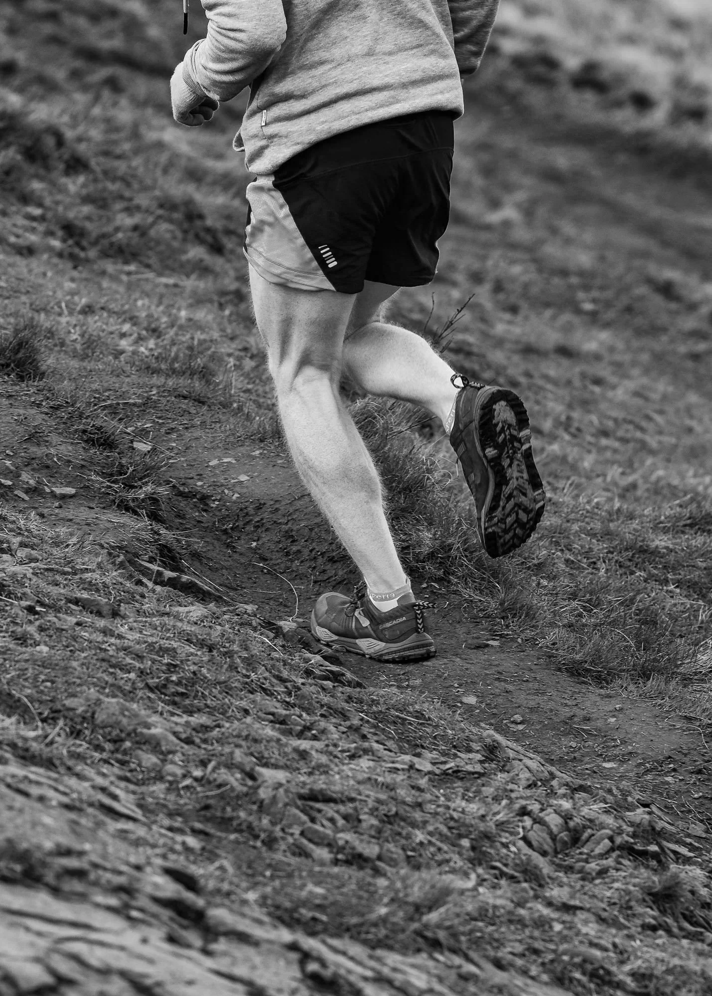 Close-up of Personal Trainer, Gregor Ridley trail running on a dirt path through a natural outdoor setting at Arthur's Seat in Edinburgh.