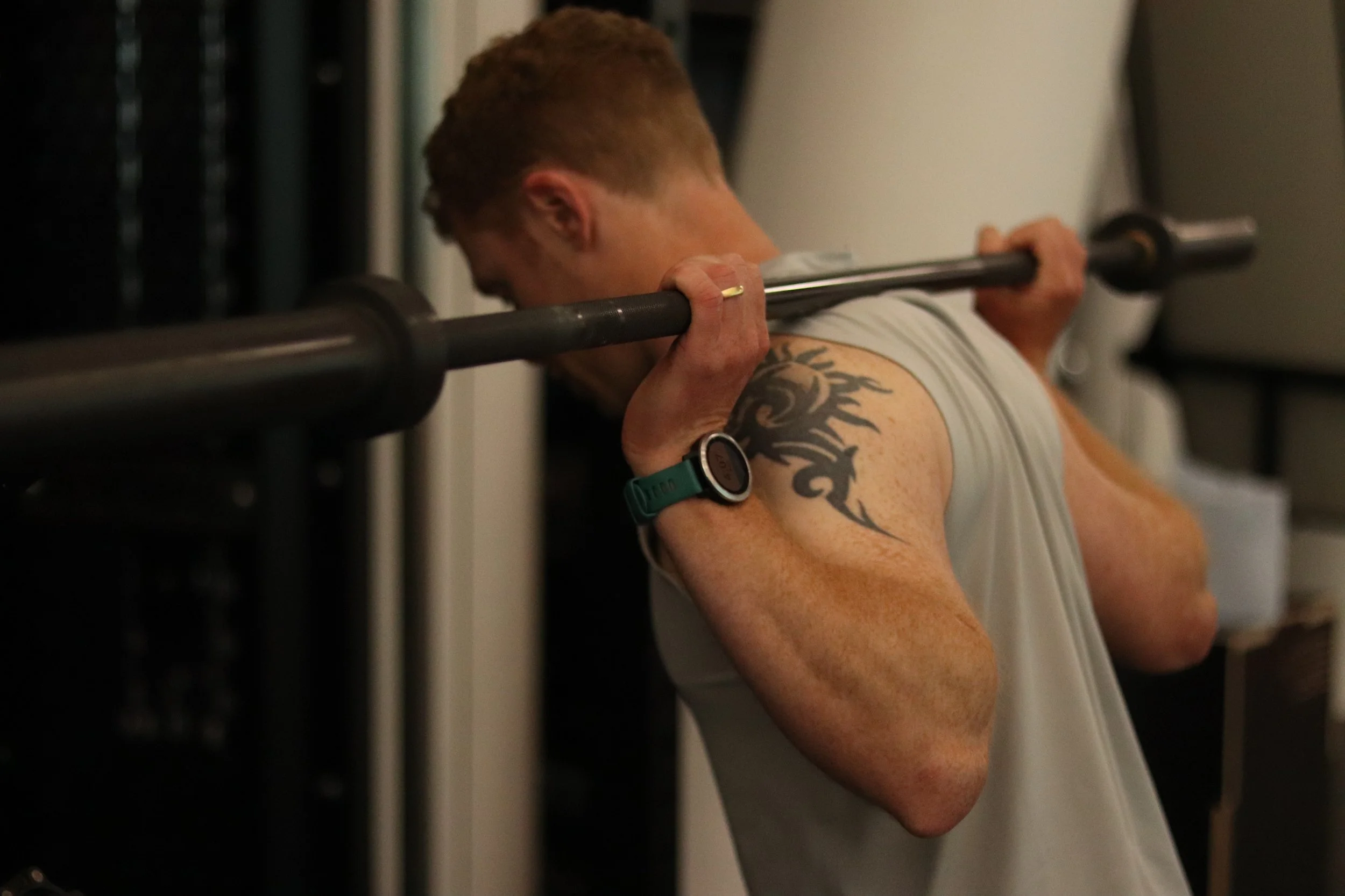 A personal trainer with 18 years of experience lifting a heavy barbell during a workout in a gym.