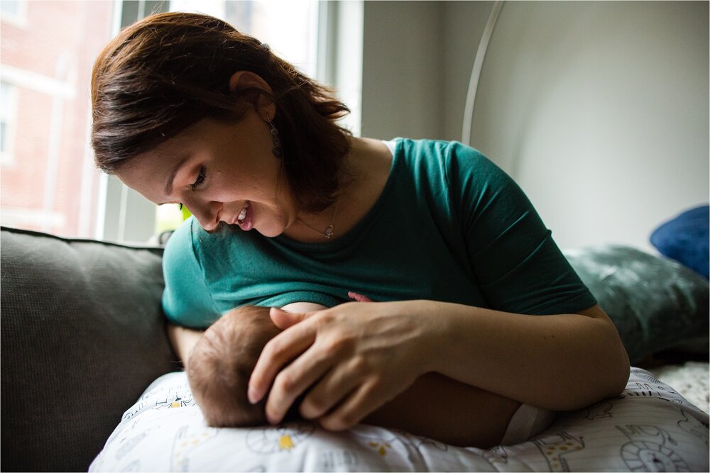 Mom breastfeeds baby boy resting on a boppy pillow, she marvels at his tiny features, portrait of a nursing mother, Philadelphia Newborn Photographer