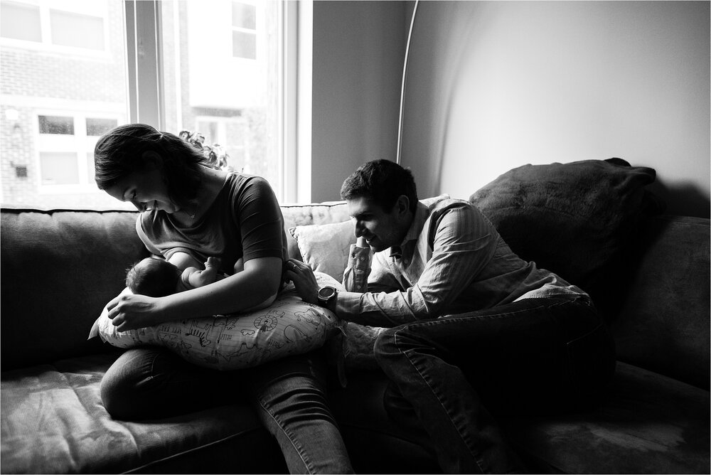 Mom breastfeeds baby boy, she marvels at his tiny features, dad tickles son's feet to keep him awake while nursing, portrait of a new family, Philadelphia Newborn Photographer