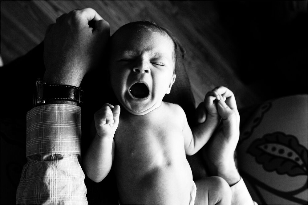 Baby boy rests on dad's lap after breastfeeding, stretches in a big yawn, Philadelphia Newborn Photography