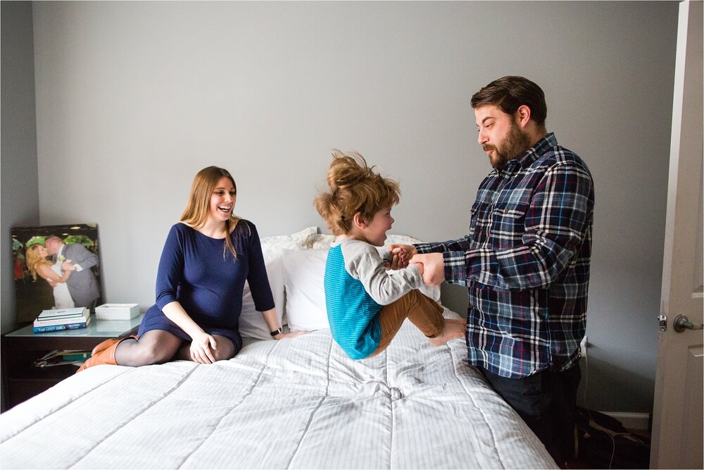 Toddler boy jumps on the bed with dad's help, dad tickles son while pregnant mom watches and laughs, Philadelphia Family Photographer