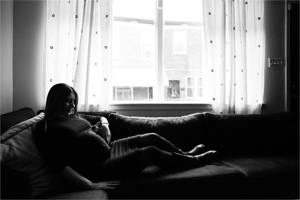 Pregnant mom sits on the couch in front of the window of her Philadelphia rowhome, black and white portrait, Philly Maternity Photographer