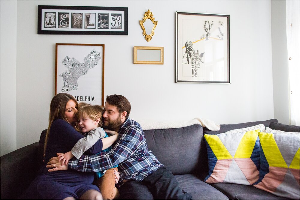 Pregnant mom and dad hug toddler son on the couch in their Philadelphia rowhome, Philly Family Photographer