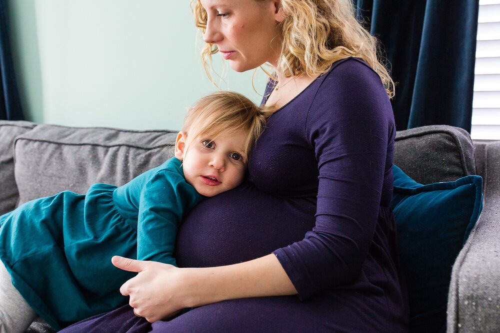 Pregnant mom in purple dress hugs toddler daughter in teal dress resting on baby belly, Philadelphia Maternity Photographer