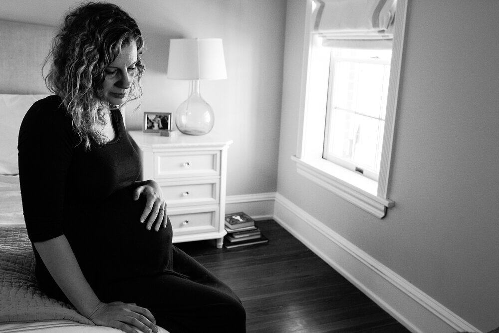 Black and white portrait of pregnant woman resting on the bed, hand on her belly, looking contemplative, Philadelphia maternity photographer