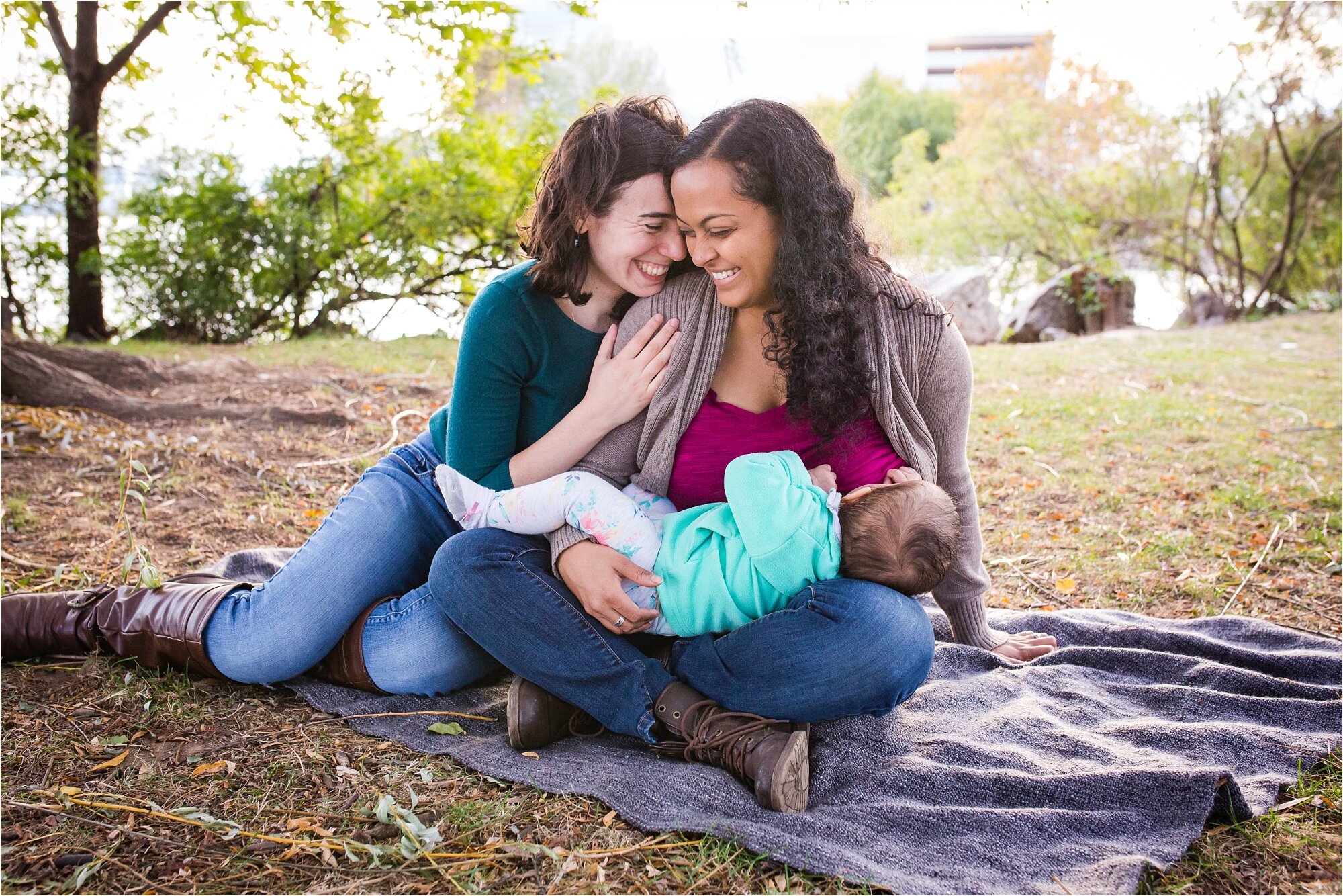 Lesbian gay mommies are sweet and laugh together while nursing their baby daughter under the willow trees by the Delaware River, Family Photography Philadelphia