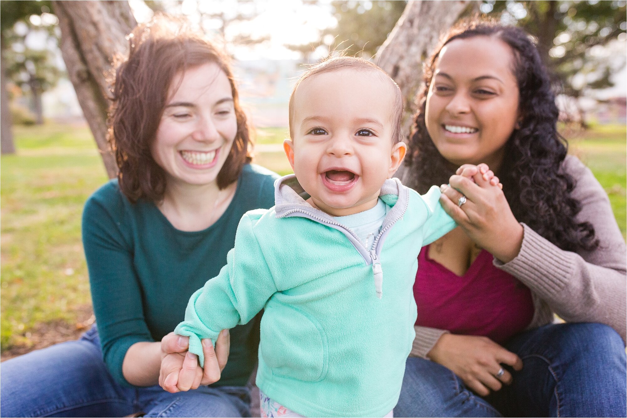 Lesbian gay mommies smile while their baby daughter laughs and looks at the camera, Family Photography Philadelphia