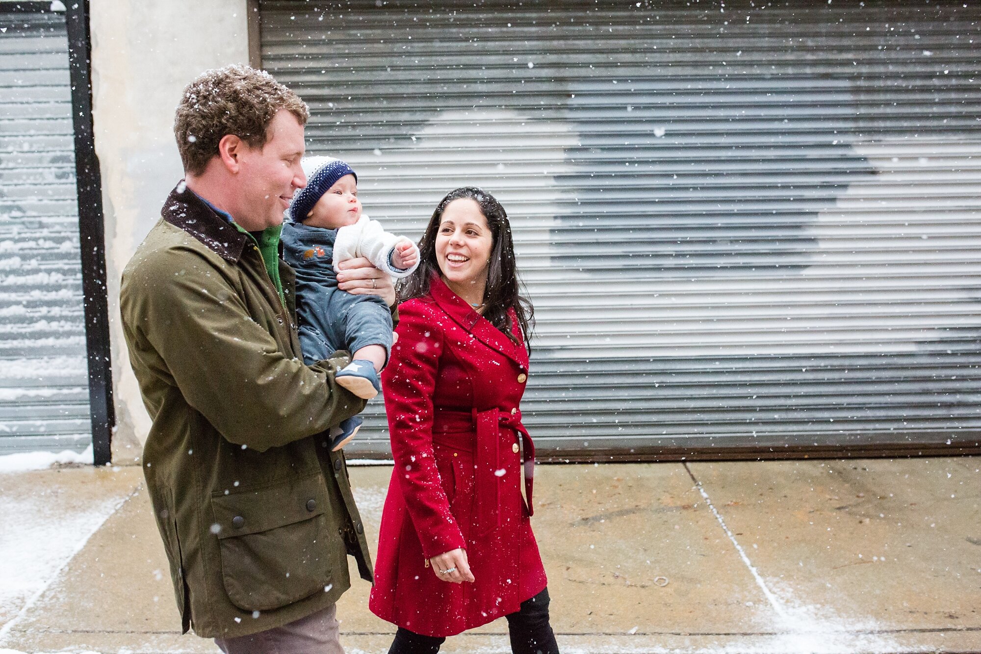 Mom, dad, and baby walk through the city through lightly falling snow, Philadelphia family photographer