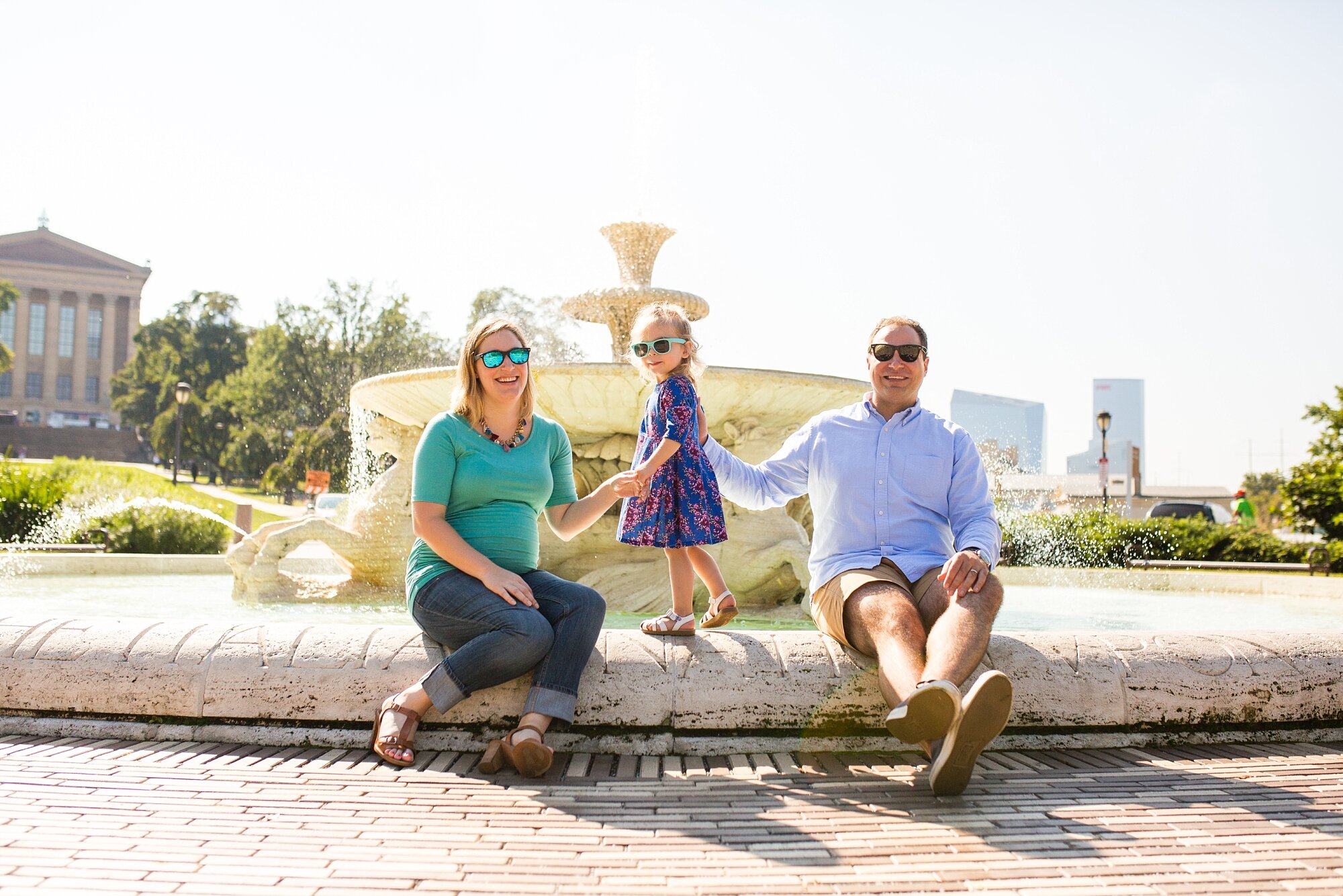 Family of three laughs and poses on the Waterworks fountain in sunglasses, Philadelphia Family Photographer