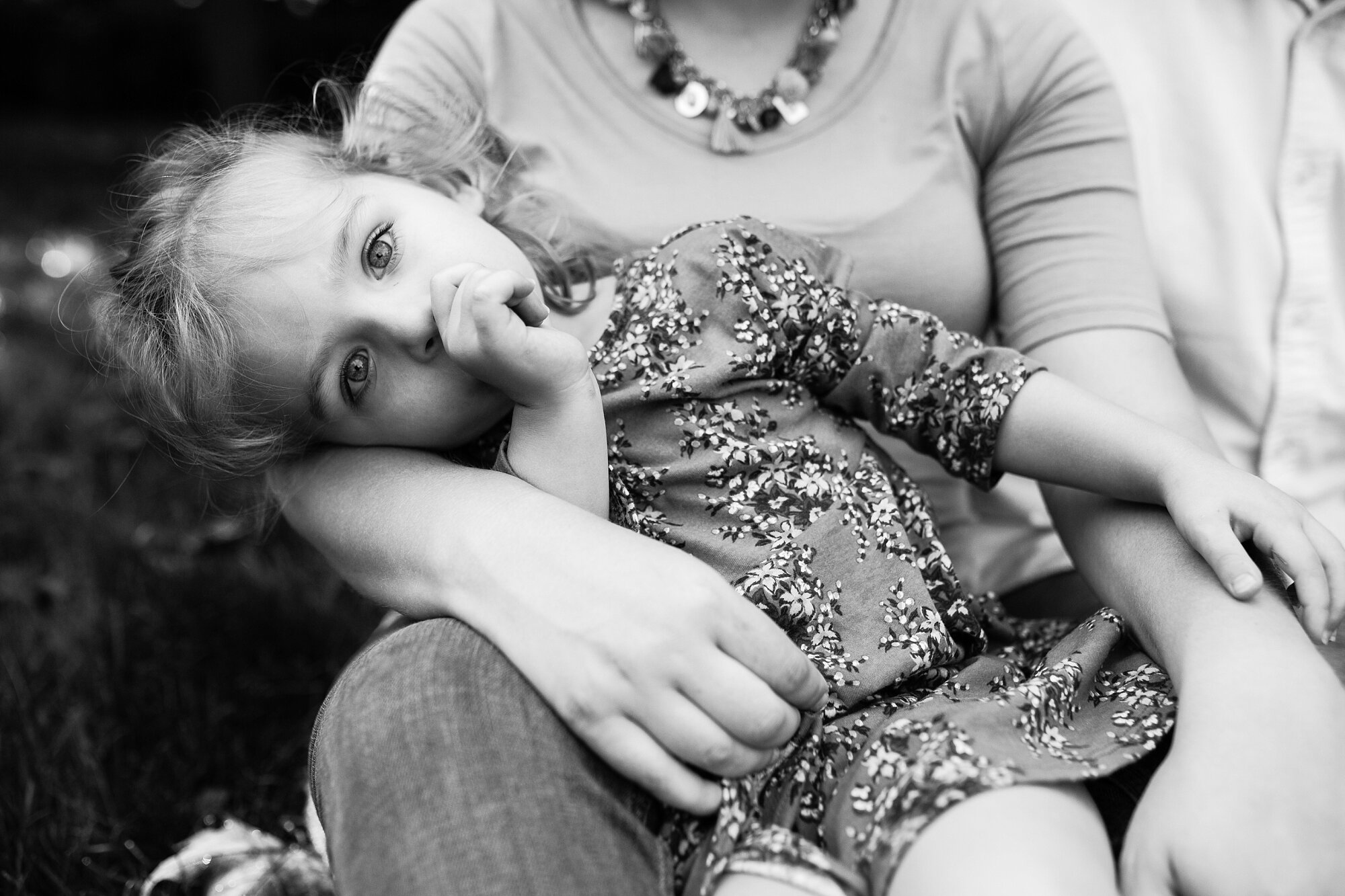 Three year old toddler rests in her pregnant mom's lap and sucks her thumb at the Azalea Gardens, Fairmount, Philadelphia Family Photographer