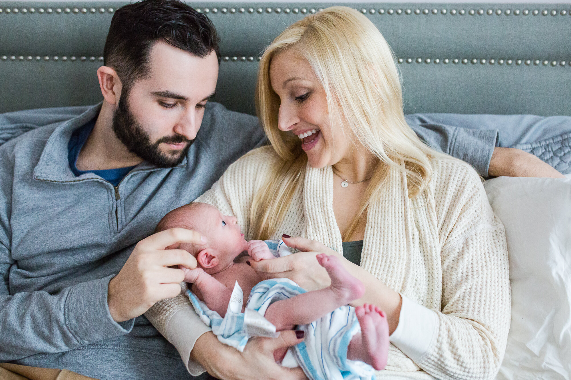 Baby boy in a blanket rests in mom's arms as she smiles at him and dad marvels at his tiny fingers, Philadelphia Newborn Photographer