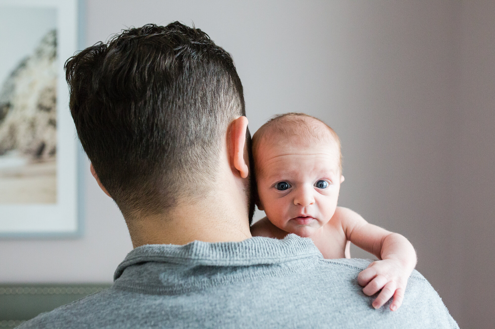 Baby boy peaks over his dad's shoulder and looks right at the camera, Philadelphia Newborn Photographer