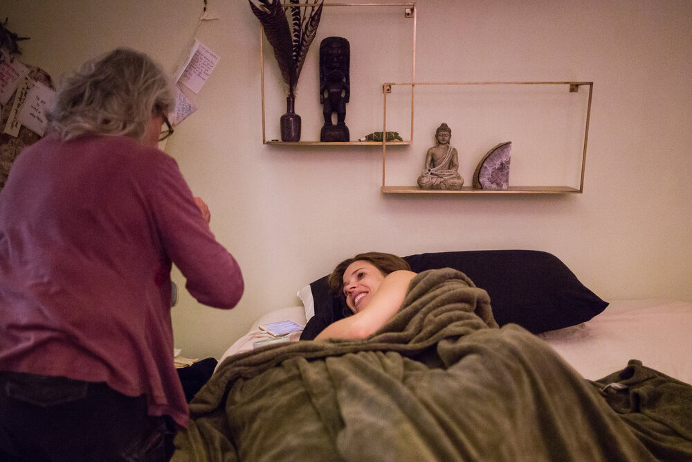 Mama rests in bed after giving birth at home as midwife takes care of her, Philadelphia birth photographer