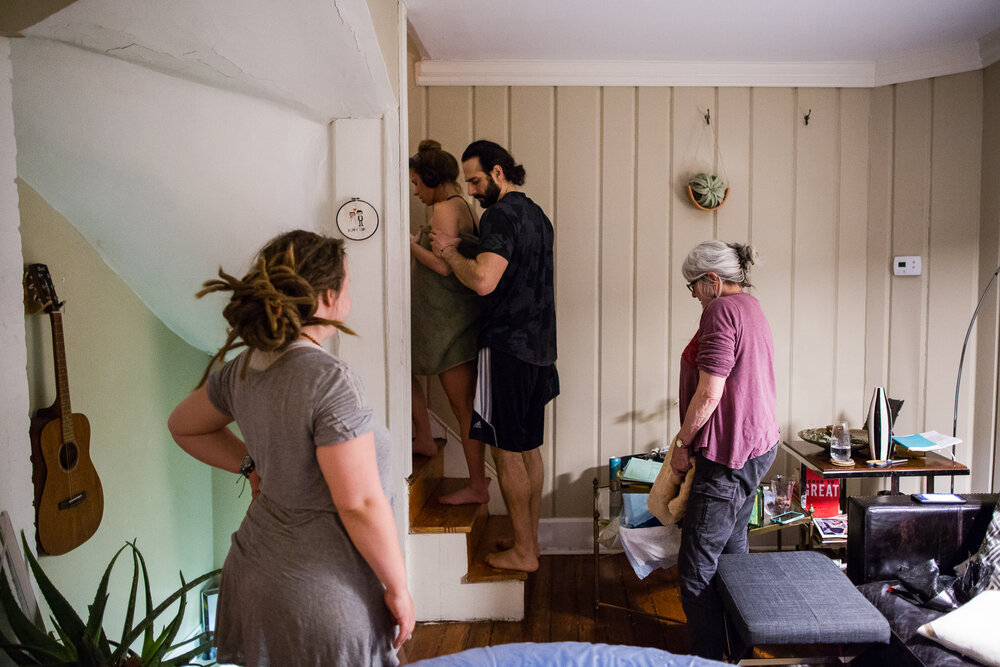 Husband helps his wife walk upstairs while she works through contractions, midwives watch and help, birth photographer Philadelphia