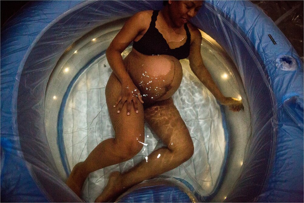 Portrait of a black mother in labor in a birth tub, water rippling over her belly, home hypnobirth Photographer Philadelphia