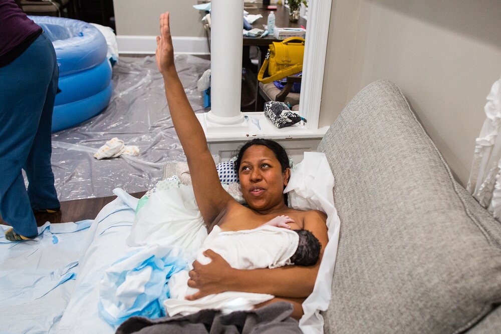 Proud black mom raises an arm in praise of her home birth, her friend doula looks amazed at her, homebirth Photographer Philadelphia