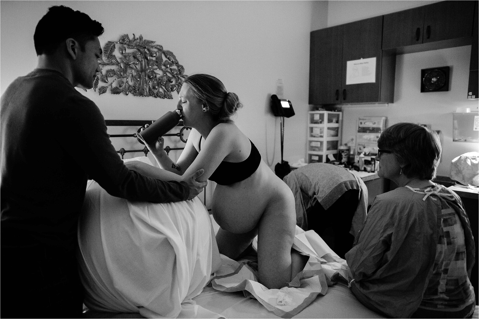 Pregnant mom drinks water in between contractions with husband's support, midwife and nurse prepare for delivery, Philadelphia birth center photography