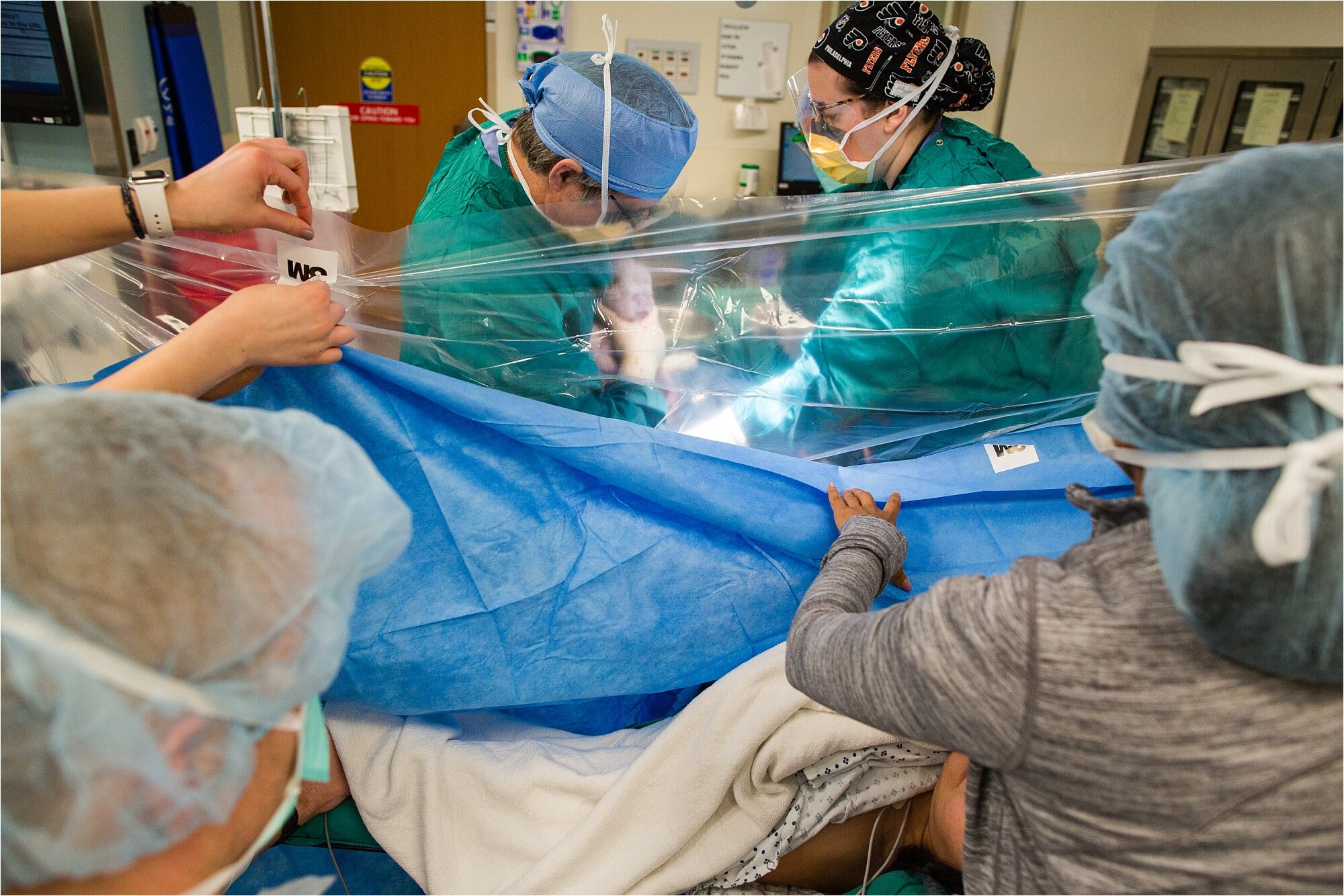 OBGYN lifts baby out of mom during c-section while the drape is pulled down so the parents can see, Philadelphia Birth Photography