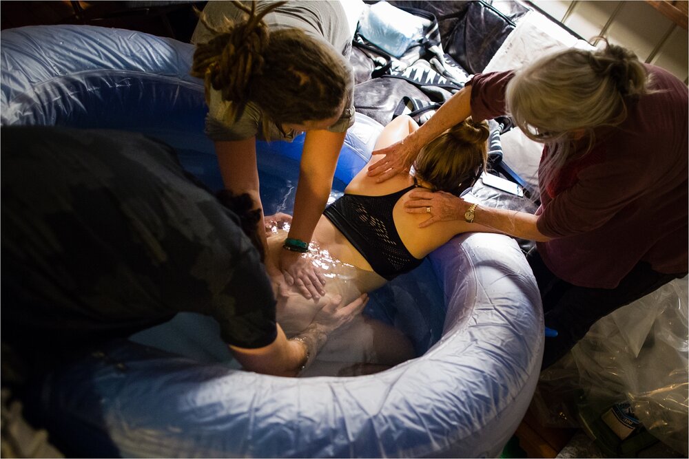 Laboring mother in birth pool gets comfort from birth team, midwives, husband, Philadelphia Birth Photographer