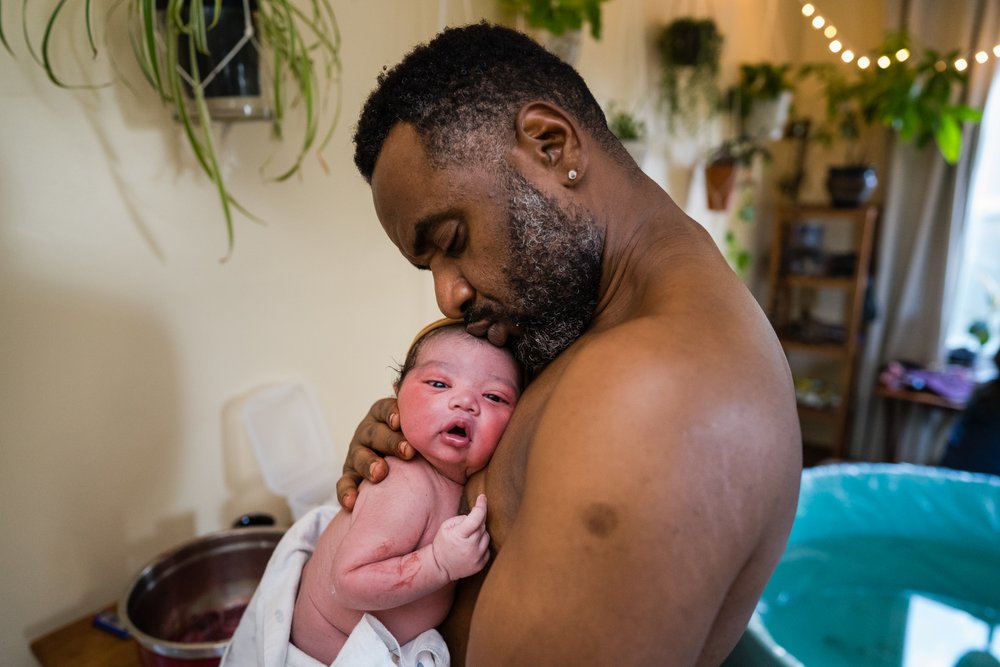 Black dad holds new son skin to skin, kisses his head, beautiful baby