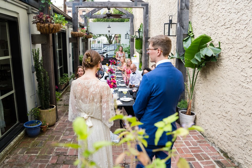 Photograph from behind bride and groom as they self-unite, guests at their small wedding seated in front of them, Philadelphia