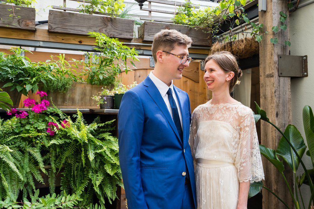 Bride and groom smile together in front of plants at Southwark Restaurant, Philadelphia