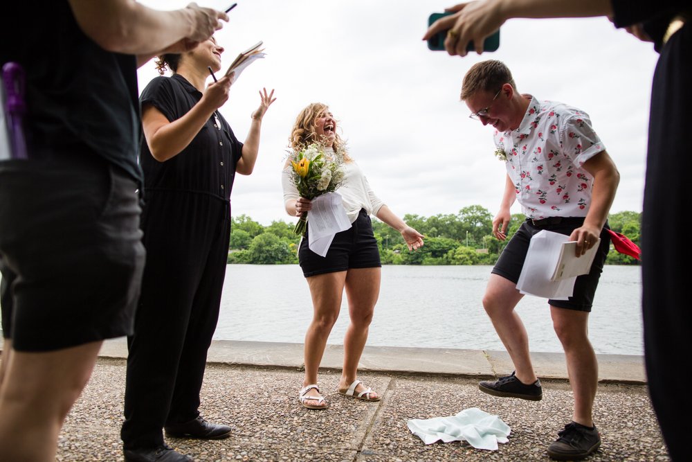 Bride laughs and friends cheer as partner stomps on and breaks wedding glass, Philadelphia photographer