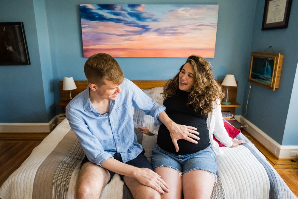 Dad touches mom's pregnant belly, colorful bedroom, in-home maternity photographer Philadelphia