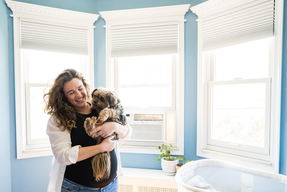 Pregnant mom looks gorgeous and so happy, snuggling her dog in soft window light, Philadelphia maternity photographer