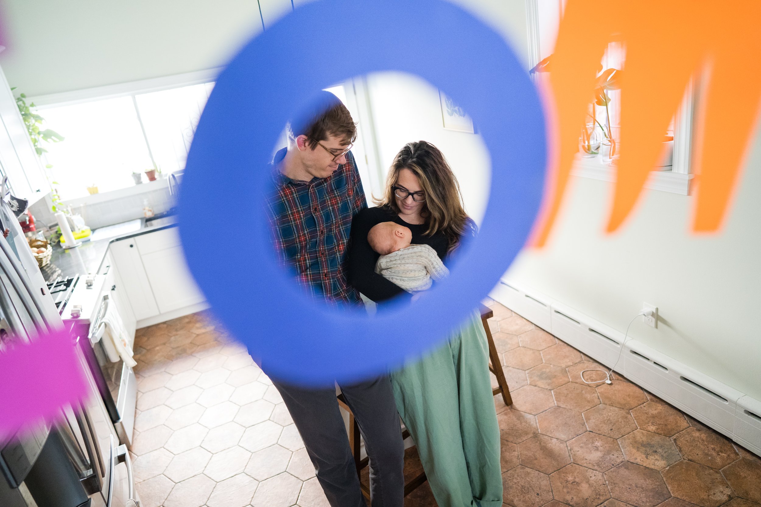 Cool shot of mom, dad, and baby through the "O" of "welcome home" sign, Philadelphia newborn photographer